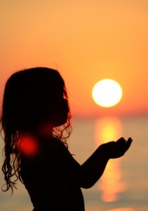 Silhouette of little girl at the sea holding the sun