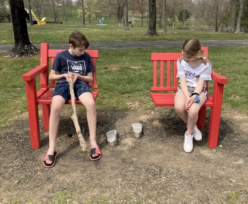 Two white, school-aged children sitting on either side of a bench that's cut in half